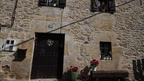 A stone building with a dark wooden door, two small windows with shutters, and a number '10' sign above the door.