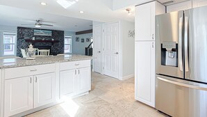 Eine geräumige Küche mit weißen Schränken, Granit Arbeitsplatten, einem Edelstahlkühlschrank und einem Wasserspender.