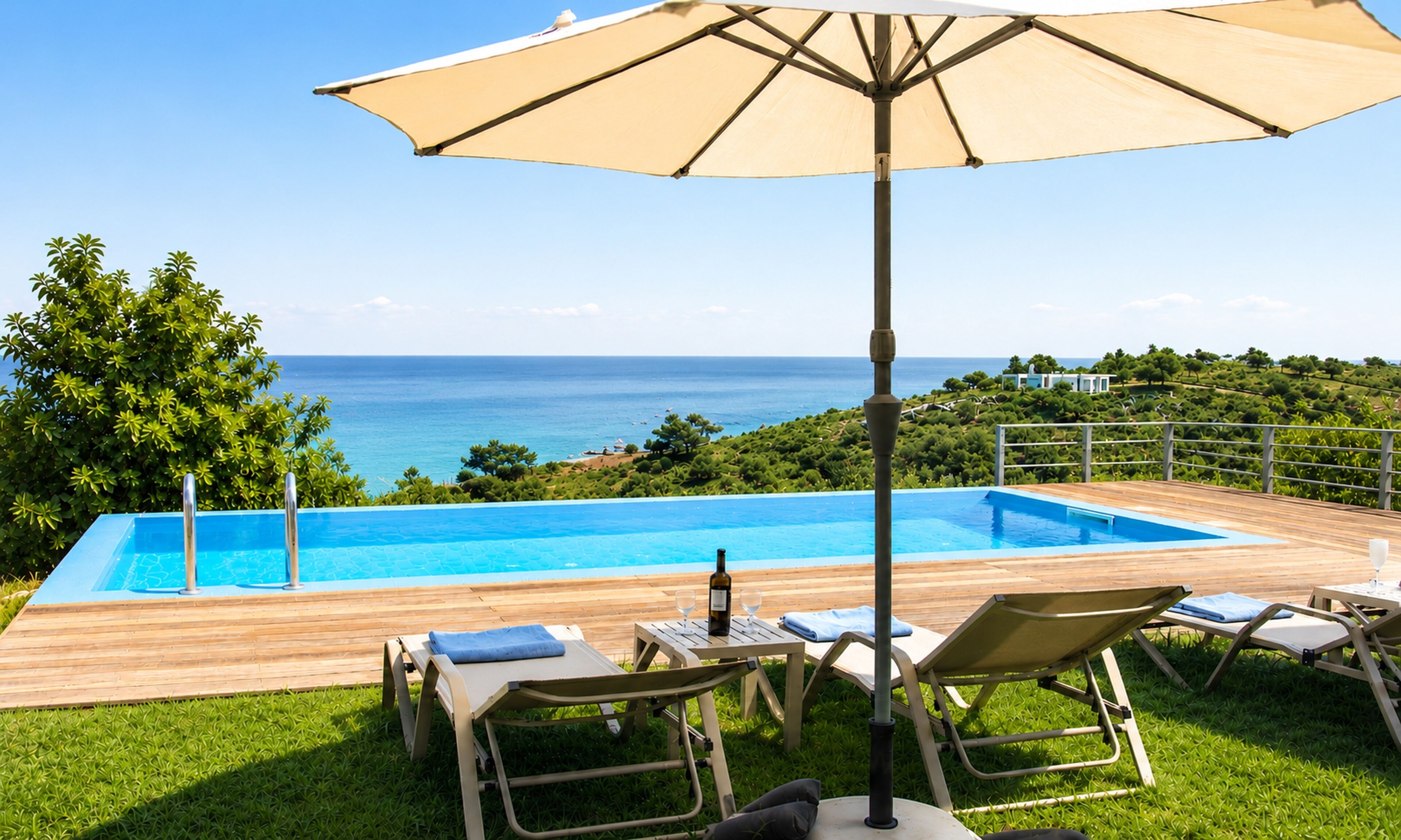 An outdoor swimming pool with lounge chairs and a table, overlooking a coastal landscape.