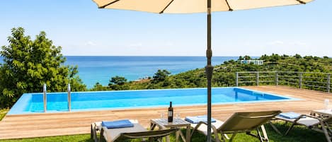 An outdoor swimming pool with lounge chairs and a table, overlooking a coastal landscape.
