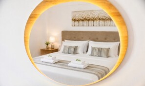 Una cama bien hecha con ropa blanca y almohadas a rayas, una mesita de noche con una lámpara y una planta pequeña, y una obra de arte colgada en la pared sobre la cama.