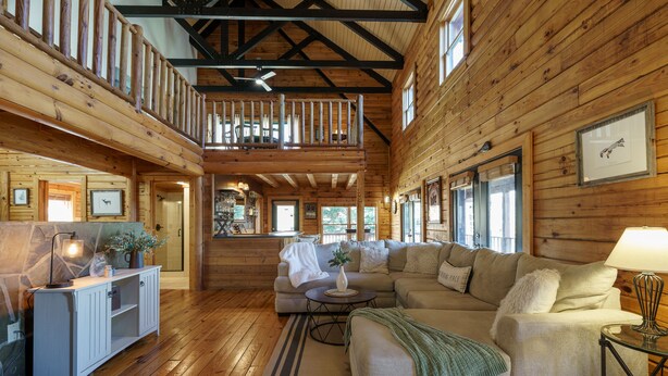 A spacious living area with a high ceiling, wooden beams, a large sofa, a coffee table, and a fireplace.
