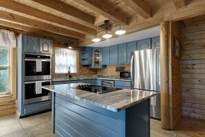A kitchen with blue cabinets, stainless steel appliances, and a wooden ceiling.