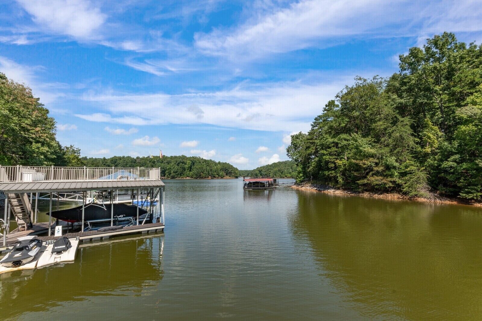 A dock with boats and a covered area, surrounded by dense trees and a calm lake.