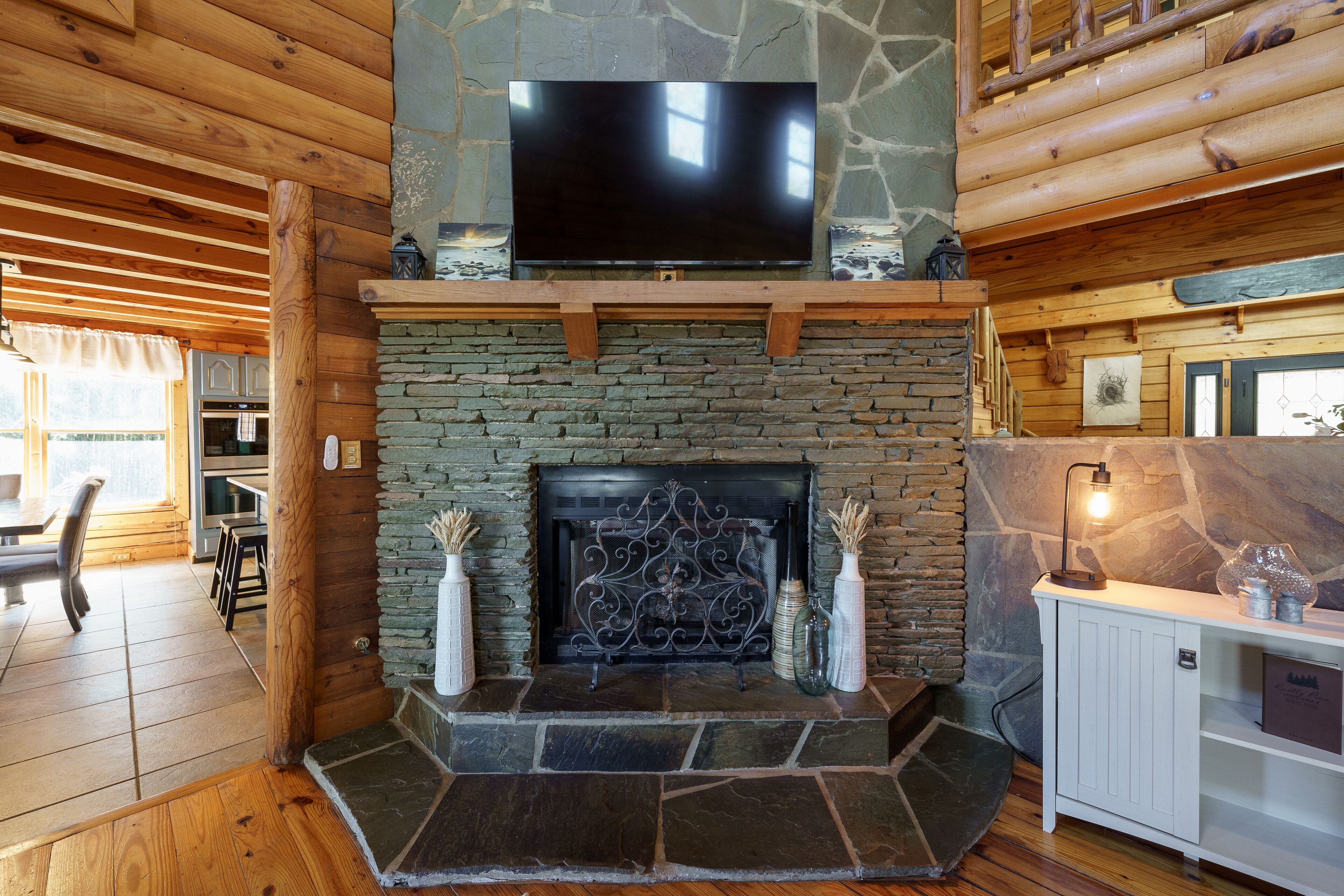 Interior acogedor de una cabaña con chimenea de piedra, televisor montado y piso de madera.