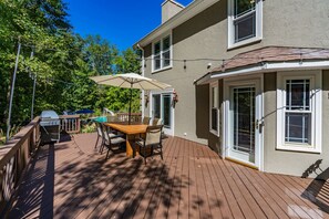 Eine Holzterrasse mit Tisch und Stühlen, einem Grill und einem Pool im Hintergrund.