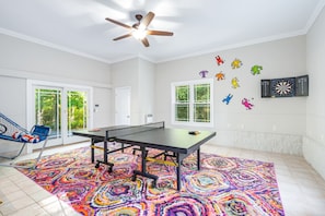 Ein Zimmer mit Tischtennisplatte, farbigem Teppich und Wandbildern.