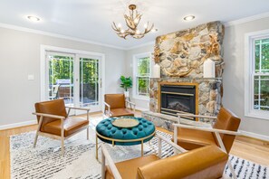 Un salon doté d’une cheminée en pierre, de fauteuils en cuir, d’un pouf rond et d’un lustre.