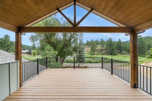 Una terraza de madera con barandilla metálica, con vistas a un paisaje boscoso.