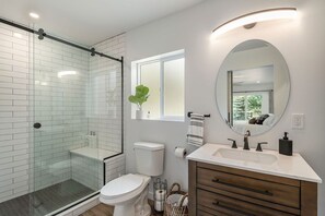 Un baño moderno con cabina de ducha de vidrio, inodoro blanco, tocador con espejo y ventana que proporciona luz natural.