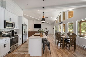 A spacious kitchen with modern appliances, a central island, and a dining area with wooden chairs. - Welcome! 4 bedroom (6 bed) 3 bath River House (Sedalia)