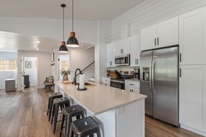 A modern kitchen with white cabinetry, stainless steel appliances, and a central island with bar stools.