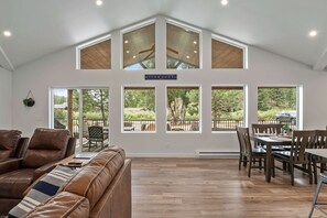 Un salon spacieux avec un plafond haut, de grandes fenêtres, un canapé en cuir et un coin repas avec des meubles en bois.
