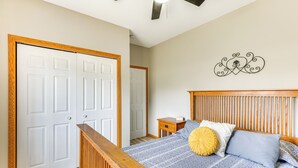Een slaapkamer met een houten hoofdbord, een bed met blauw-witte beddengoed, een geel accentkussen en een decoratief object aan de muur.