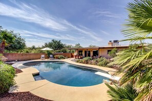 A swimming pool with a curved edge, surrounded by a landscaped garden and a patio area with outdoor furniture. - Stylish Tucson Home w/ Patio & Private Pool! (Tucson)
