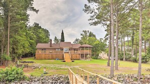 A lodge with a wooden deck over a pond, surrounded by trees.