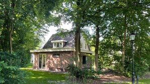 Una casa de maó amb teulada inclinada, envoltada de vegetació i arbres frondosos.