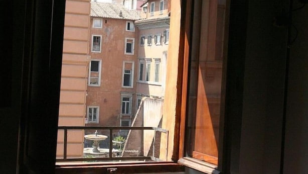 A view from a window with a balcony, overlooking a row of buildings with uniform architecture and a small fountain in the foreground. - Portico d'Ottavia, heart of ancient Rome (Roma)