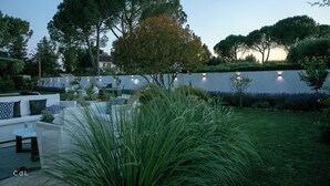 A serene outdoor patio area with a white sofa set, a small table, and a decorative wall with lights.
