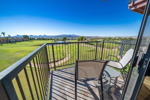 Uma varanda com vista para um campo de golfe, uma cadeira e uma mesa.