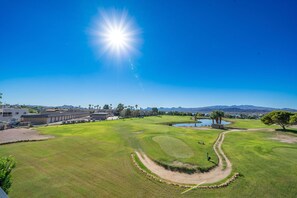 Um campo de golfe com céu limpo, um lago e montanhas ao longe.