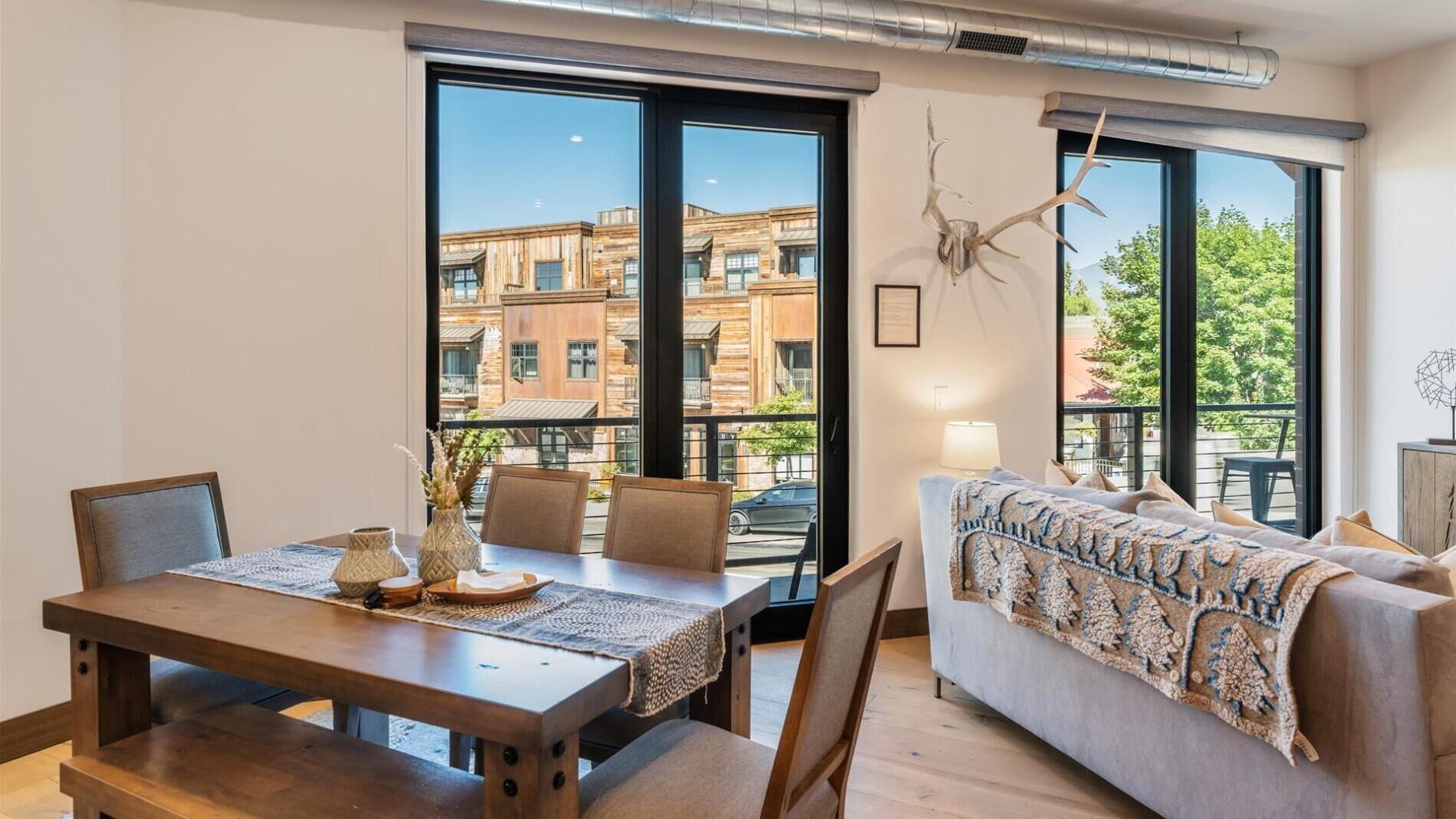 A modern living room with a dining area, large windows, and a view of a building with brickwork.