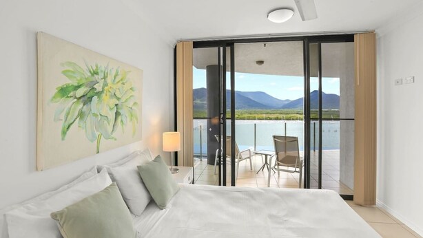 Ein Hotelzimmer mit einem großen Bett, einem Bild an der Wand und einem Balkon mit Blick auf Berge und Wasser.