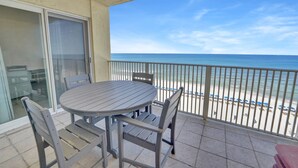 A balcony with a table and chairs, overlooking a beach with umbrellas.