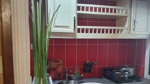 Uma cozinha com azulejos vermelhos no painel atrás do fogão, armários brancos, um vaso de vidro com hastes verdes e panelas sobre o fogão.