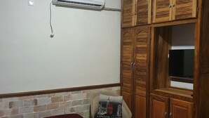 Quarto com cama, guarda-roupa de madeira, televisão e ar condicionado.