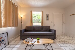 Een woonkamer met een grijze bank, een houten salontafel en een kleine plant in pot.