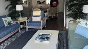 Ein Wohnzimmer mit einem weißen Couchtisch, blaugrünen Sofas, einem Essbereich mit einem Stuhl und einer Küche im Hintergrund.
