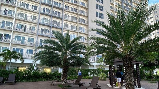 Hotellissa on uima-allas, aurinkotuoleja, palmuja ja suuri rakennus taustalla.