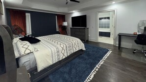 A modern bedroom with a bed, a desk, a chair, a ceiling fan, and a TV.