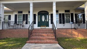 A two-story house with a front porch, brick steps, and a green door.