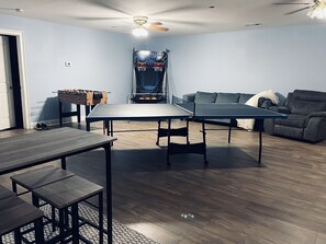 Una habitación con mesa de ping pong, mesa de futbolín, sofá y ventilador de techo.