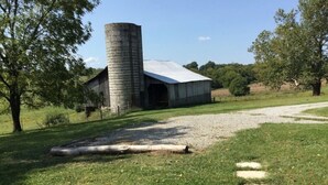 A rustic barn with a silo, surrounded by a grassy field and trees.