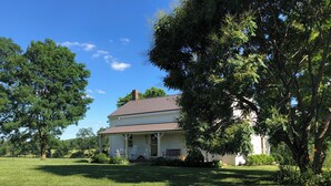 A two-story house with a porch, surrounded by a grassy lawn and trees.