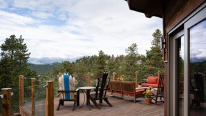 A wooden deck with outdoor furniture, including a table, chairs, and a sofa, overlooking a mountainous landscape. - Spacious 4 BR mountain home with pool table, hot tub, and incredible views (Golden)