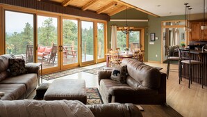 A spacious living room with a large sliding glass door leading to a deck, a cozy seating area with a fireplace, and a kitchen area with bar stools. - Spacious 4 BR mountain home with pool table, hot tub, and incredible views (Golden)