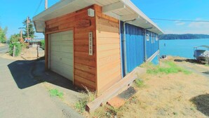 Un pequeño edificio de madera con una puerta de garaje, un letrero que dice “Welcome to The Comans” y el número “24480” en el lateral.