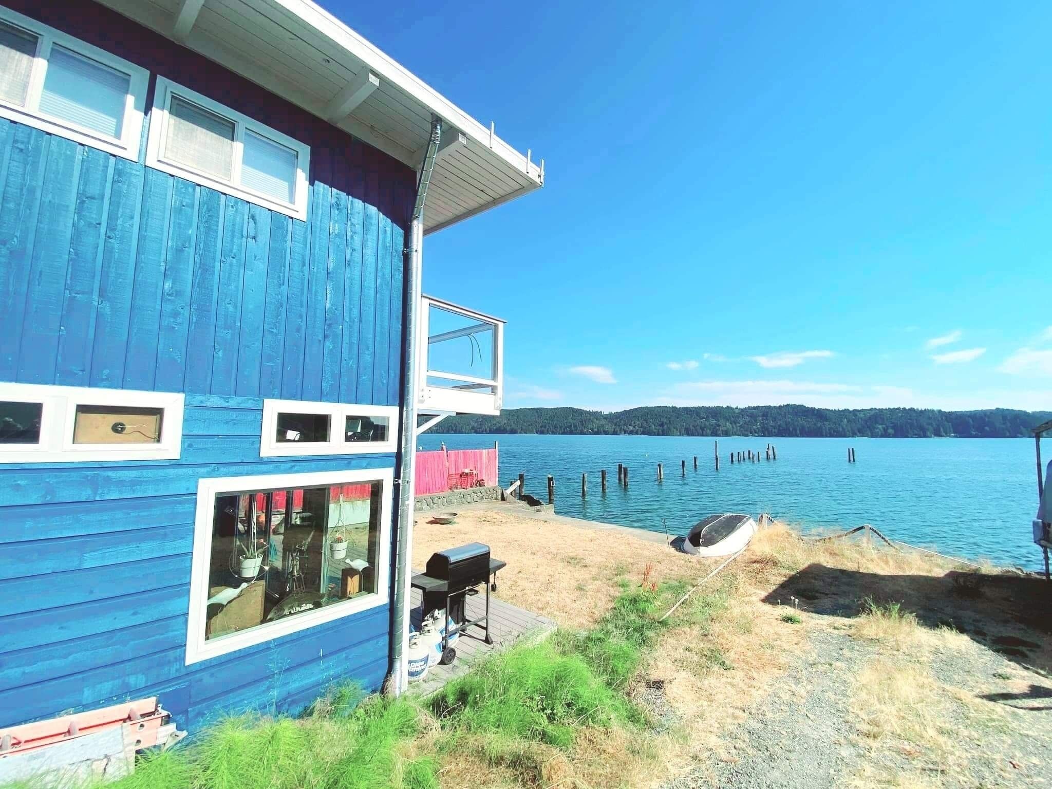 A blue house with a deck overlooking a lake, a barbecue grill, and a fishing rod.