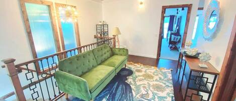 A green sofa in a room with a patterned rug, wooden ceiling, and a staircase.