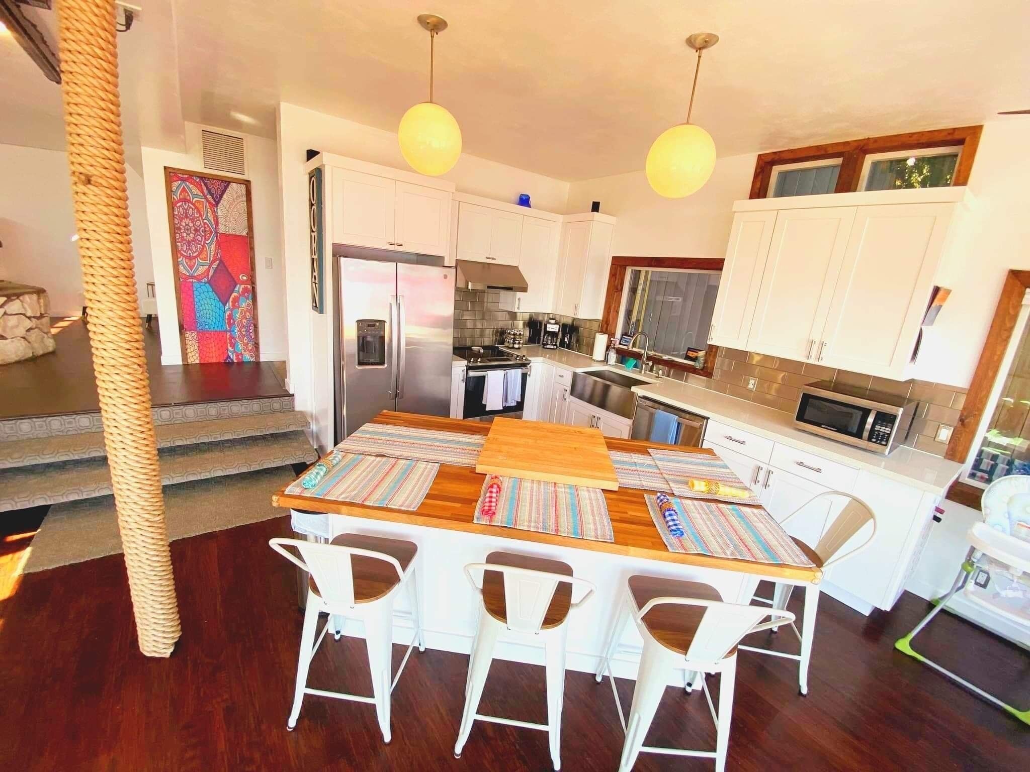 A modern kitchen with white cabinets, stainless steel appliances, and a wooden dining table with striped placemats.