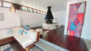 Una sala de estar moderna con chimenea de piedra, un sofá blanco con cojines estampados y un cuadro abstracto y colorido en la pared.
