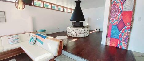 A modern living room with a stone fireplace, a white sofa with patterned cushions, and a colorful abstract painting on the wall.