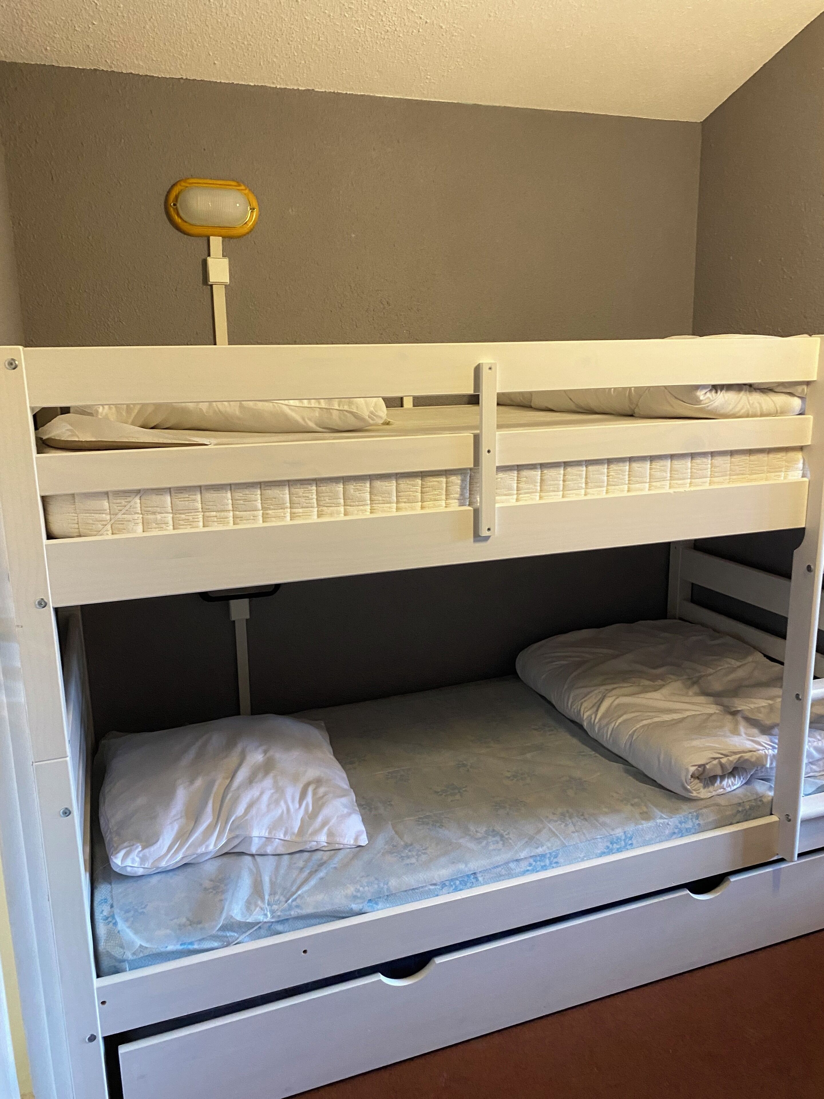 A bunk bed with a mattress on the top bunk and a lower bunk with a storage drawer.