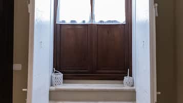 Una scala conduce a una porta di legno scuro con una tenda bianca. Due cesti bianchi sono posizionati sui gradini.