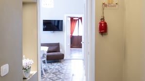 A hallway leading to a living area with a sofa, a TV mounted on the wall, a patterned floor, and a red bell on the wall. - TRESCA CHARME ROOM 22  (Bari)