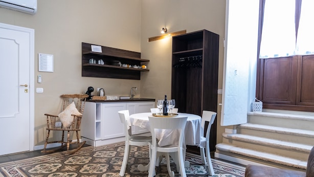 A compact kitchen with white cabinetry, a dining area with a round table and chairs, a patterned floor, and a staircase leading to a dark wooden door. - TRESCA CHARME ROOM 22  (Bari)